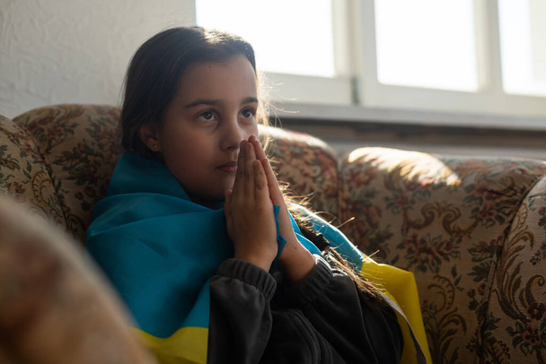 mała dziewczynka uchodźca modli się z ukraińską flagą. - Zdjęcie, obraz