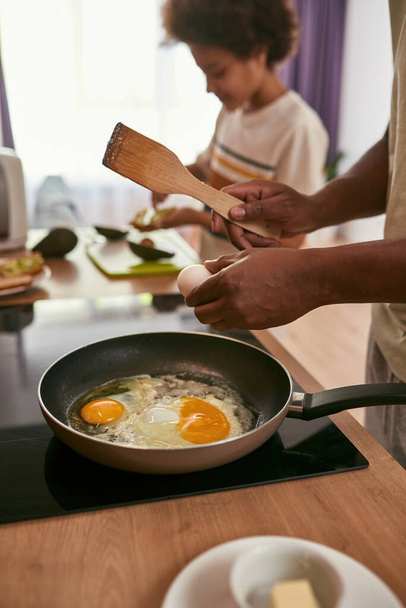 Man fry eggs on pan and son smear kiwi on bread - Foto, afbeelding