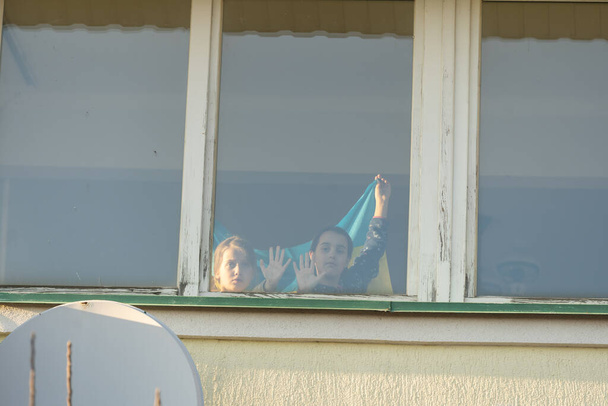 Niño en la ventana con la bandera de Ucrania. Apoyo estatal en la guerra. Guardar Ucrania concepto - Foto, imagen