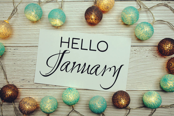 Hello January text on paper card with cotton ball LED decoration on wooden background - Фото, изображение