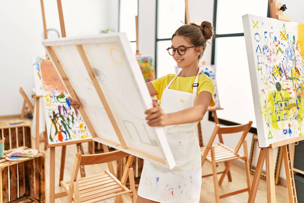 Urocza dziewczyna uśmiechnięta pewnie patrząc płótno rysować w studio sztuki - Zdjęcie, obraz