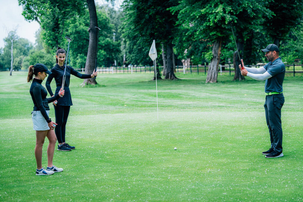 A aprender golfe. Instrutor de golfe com mulheres jovens em um campo de golfe - Foto, Imagem
