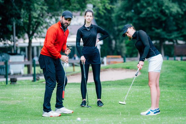 Урок покладання гольфу, дві молодих гольфісток практикують покласти з інструктором гольфу
 - Фото, зображення
