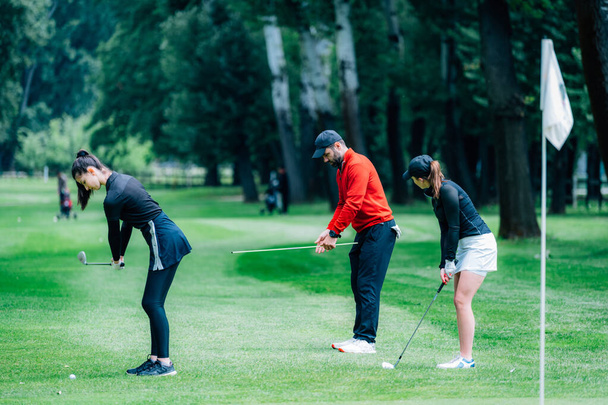 Двоє молодих гольфістів практикують постріли на полі для гольфу з інструктором гольфу
 - Фото, зображення