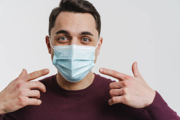 Young brunette man pointing fingers at his face mask isolated over white background - Photo, Image