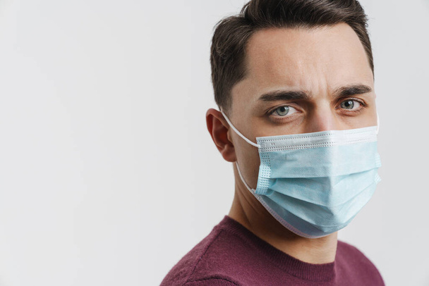 Young brunette man in face mask posing and looking at camera isolated over white background - Foto, afbeelding