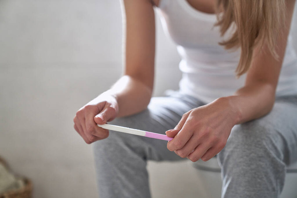 Unerkennbare Frau sitzt und hält Schwangerschaftstest  - Foto, Bild