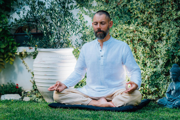 Medytuję, człowieku. Spokojny człowiek siedzący w pozycji lotosu i medytujący w ogrodzie. - Zdjęcie, obraz