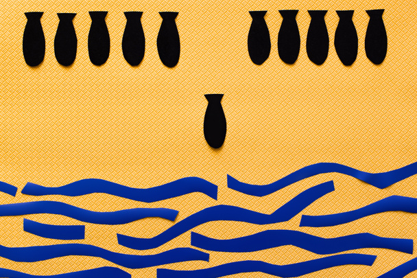 Bovenaanzicht van papieren bommen boven abstracte kartonnen zee op getextureerde gele achtergrond  - Foto, afbeelding
