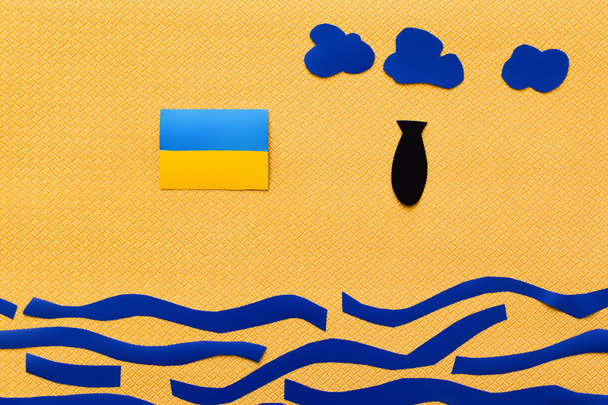 Top view of ukrainian flag and paper bomb above carton sea on textured yellow background  - Zdjęcie, obraz
