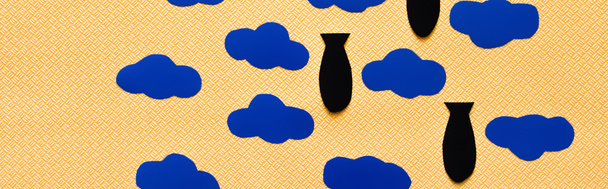 Top view of paper bombs and carton clouds on textured yellow background, banner  - Zdjęcie, obraz