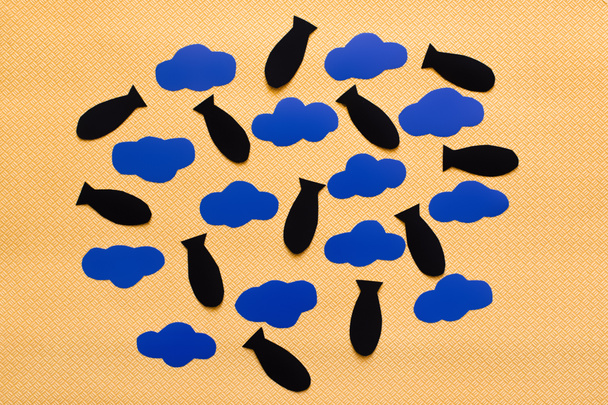 Top view of blue carton clouds and paper bombs on textured yellow background  - Photo, Image