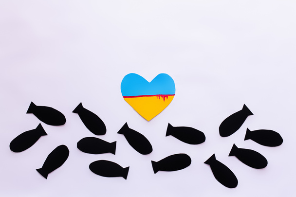 Top view of ukrainian flag with blood in heart shape near paper bombs on white background  - Foto, Imagen