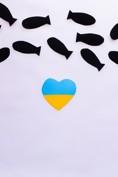 Bovenaanzicht van Oekraïense vlag in hartvorm onder papieren bommen op witte achtergrond  - Foto, afbeelding