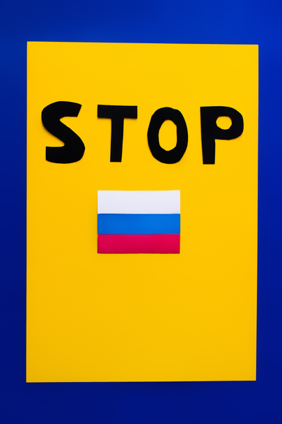 Κάτοψη του stop lettering και ρωσική σημαία σε μπλε και κίτρινο φόντο  - Φωτογραφία, εικόνα