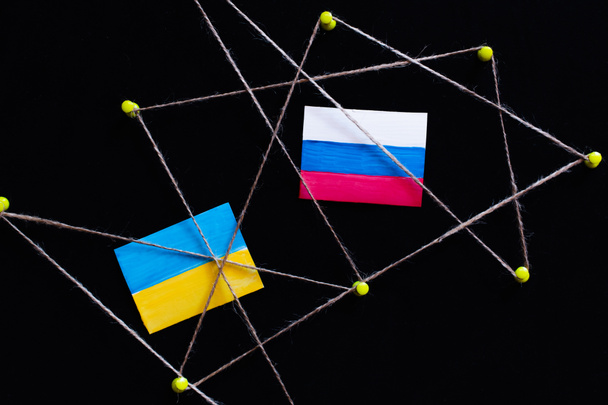 Top view of push pins with thread, ukrainian and russian flags isolated on black  - Foto, immagini