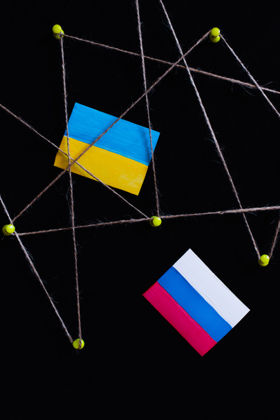 Widok z góry flagi ukraińskiej i rosyjskiej w pobliżu szpilki z nitką izolowane na czarno - Zdjęcie, obraz