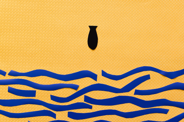 Вид сверху бумажной бомбы над картонным морем на текстурированном желтом фоне, война в концептуальном виде  - Фото, изображение