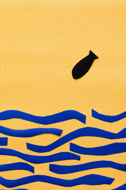 Верхній вид паперової бомби над картонним синім морем на текстурованому жовтому тлі, війна в українській концепції  - Фото, зображення