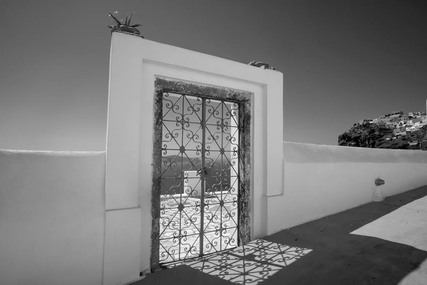 Внешняя украшенная дверь с цветочными растениями на крыше виллы и вид на Эгейское море в Фира Санторини в черно-белом цвете  - Фото, изображение