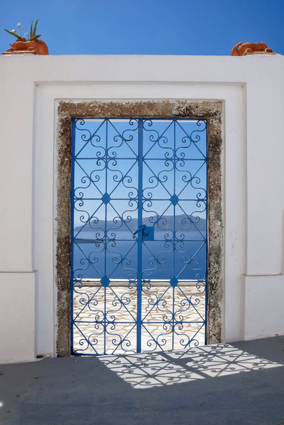 Zewnętrzne ozdobione drzwi z kwiatami na dachu willi i widokiem na morze Morza Egejskiego w Fira Santorini - Zdjęcie, obraz