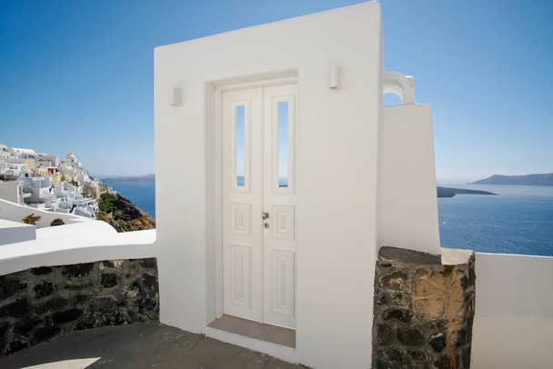 Typowy design białe drzwi dekoracyjne obok alejki z zapierającym dech w piersiach widokiem na wioskę Fira i Morza Egejskiego w Santorini - Zdjęcie, obraz