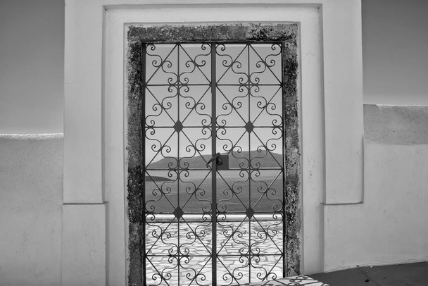 Zewnętrzne ozdobione drzwi z kwiatami roślin na dachu willi i widok na morze Morza Egejskiego w Fira Santorini w czerni i bieli - Zdjęcie, obraz