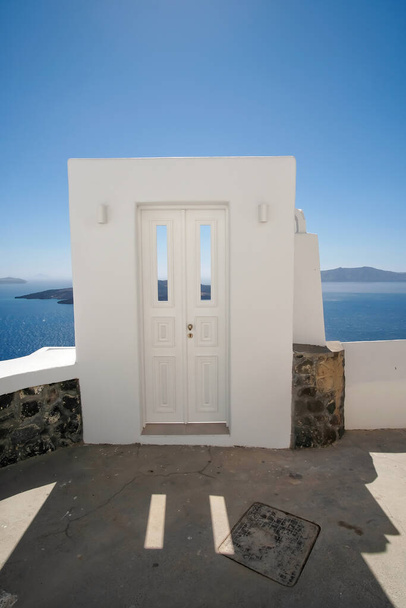 Типовий дизайн дверей білого орнаменту поруч з алеєю з захоплюючим видом на море егейського моря в Санторіні. - Фото, зображення