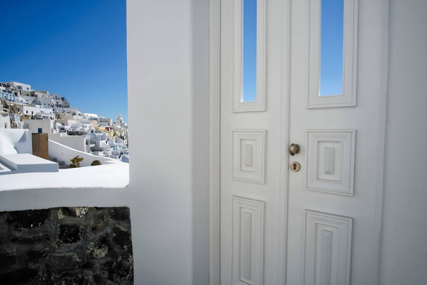 Típica puerta de decoración blanca de diseño junto a un callejón con una vista impresionante del pueblo de Fira y el mar Egeo en Santorini - Foto, imagen