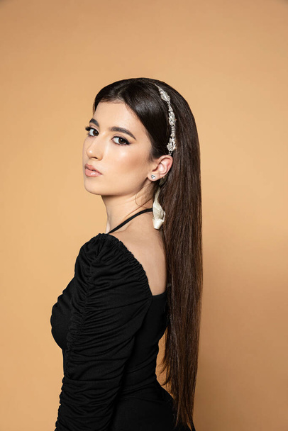 Érzéki kaukázusi nő modell egyenes haj fekete ruha pózol profil, izolált bézs háttér. - Fotó, kép