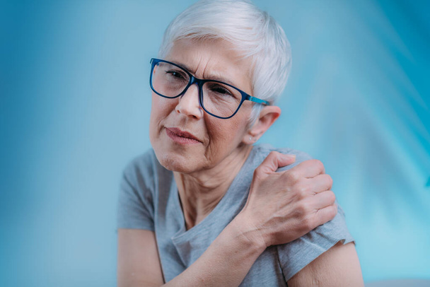 Bevroren schouder. Oudere vrouw met koud kompres, ijszak op haar pijnlijke schouder - Foto, afbeelding