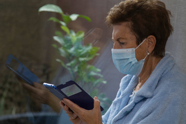lonely senior person with medical mask and mobile phone at the window - Foto, immagini