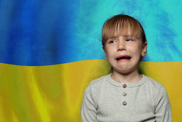 Crying child girl against Ukrainian flag background. Stop war in Ukraine - Photo, Image