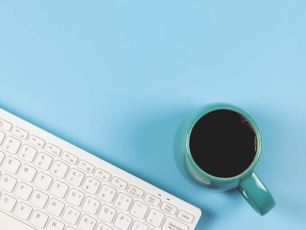 Draufsicht oder flache Lage der Computertastatur, blaue Tasse schwarzen Kaffees auf blauem Hintergrund mit Kopierraum für Text. Weiblicher Arbeitsplatz, morgendliche Routine. - Foto, Bild