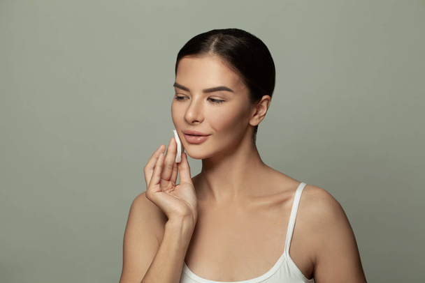 Attractive woman removing makeup with white cotton pad on gray background - Photo, Image