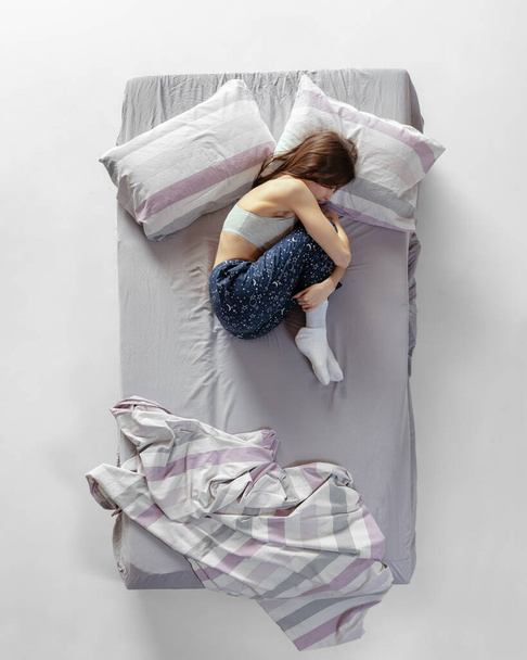 Effrayé. Portrait de la jeune fille en tenue de maison, pyjama dormant dans un grand lit gris. Concept de santé, intérieur de la maison, temps de détente, famille, rêves - Photo, image