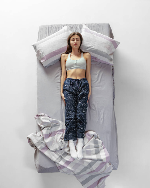 Top view portrait of young girl wearing homewear, pajamas sleeping in big gray bed. Concept of health, home interior, relax time, family, dreams - Foto, Bild
