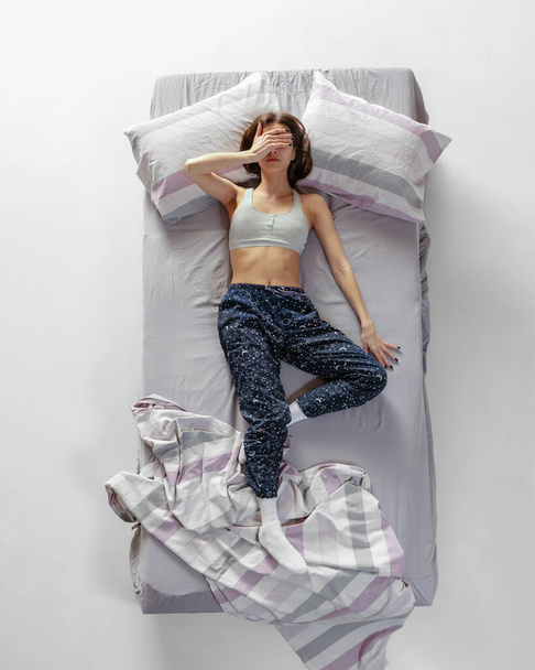Retrato de vista superior de menina vestindo roupa de casa, pijama dormindo em grande cama cinza. Conceito de saúde, casa interior, tempo de relaxamento, família, sonhos - Foto, Imagem