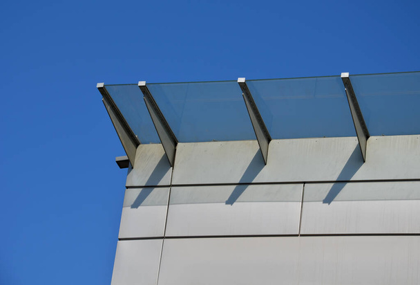 Lasikatto teollisuusrakennuksen sisäänkäynnin yläpuolella julkisivun metallipinnoitteella. paksuseinäinen lasi paneeli roikkuu oven yläpuolella metallitangot pyöreä tavoitteet haltijat, sininen taivas - Valokuva, kuva