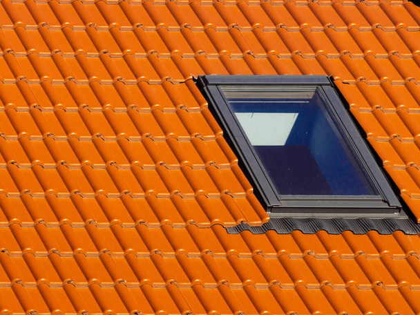 Παράθυρο στην οροφή του σπιτιού με πορτοκαλί κεραμίδια οροφής σε ένα φόντο του μπλε ουρανό άνοιξη. Υψηλής ποιότητας φωτογραφία - Φωτογραφία, εικόνα