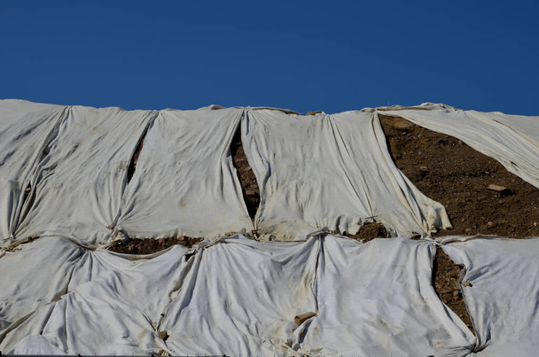 Tijdelijke afdekking van het gazon zaaiweefsel om een grote helling tegen erosie te garanderen. Langs de houten trap. met een bruine jute stof die het kokosnet stabiliseert voor steile hellingen. in de regen  - Foto, afbeelding