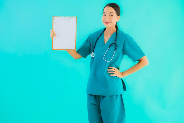 Portrait beautiful young asian doctor woman with empty paper board for copy space on blue isolated background - Healthcare in hospital and clinic concept - Photo, Image