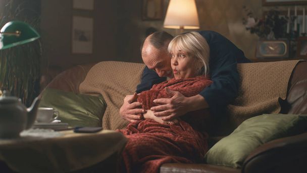 Senior man hugging surprised woman on couch - Fotó, kép