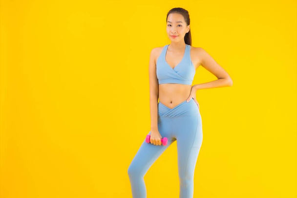 Portré gyönyörű fiatal ázsiai nő súlyzóval és sportruházat kész gyakorolni sárga elszigetelt háttér - Fotó, kép