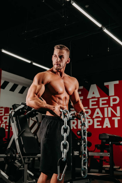 Succesful sportsman shows his body and results of trainings and posing with chains in special grung background. - Фото, зображення