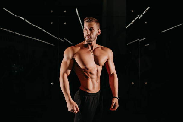 Contrast Portrait of Confident Thinking Caucasian Bodybuilder Athlete Man Posing With Lifted Hand With Naked Torso Against Dark Background.Horizontal Shot - Photo, Image