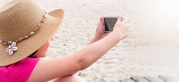 girl with hat  making a selfie with mobile phone on the beach - Valokuva, kuva