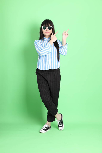 The young Asian girl with sunglasses standing on the green background. - Photo, image