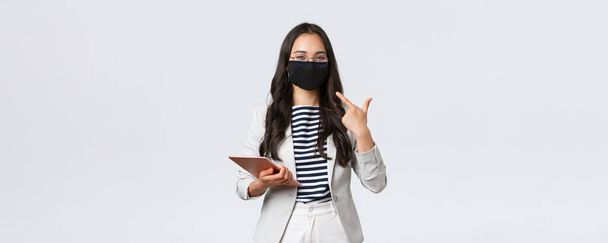 Business, finance and employment, covid-19 preventing virus and social distancing concept. Smiling asian businesswoman with digital tablet pointing at protective mask on face - Fotografie, Obrázek