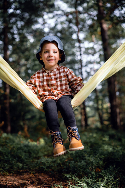 Small kid in yellow hammock in autumn forest - Fotoğraf, Görsel